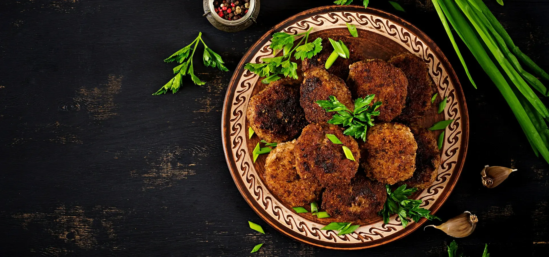 Talerz smażonych kotletów mielonych podanych z natką pietruszki i szczypiorem na ciemnym drewnianym tle